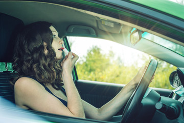 Fototapeta premium Driver woman looking in mirror and lipstick in car. Distracted and dangerous driving. The traffic violation