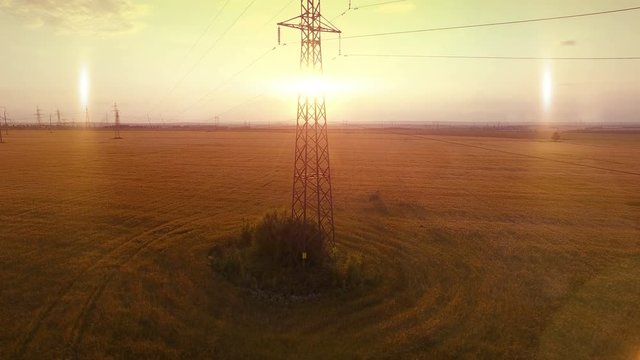 AERIAL High-voltage tower summer warm evening light camera fly up near metal structure contour opposite sun