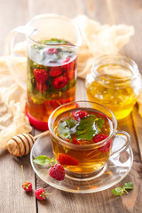 Glass cup of hot tea with raspberries, mint and honey