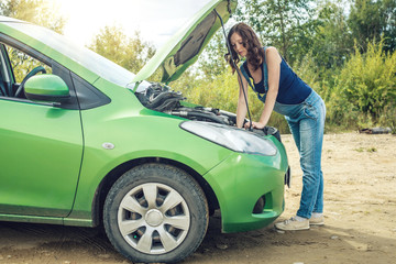 Young woman looking into the open hood. Car needs a repair