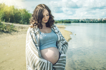 Pregnant walks on the river shore. Wrapped in a blanket