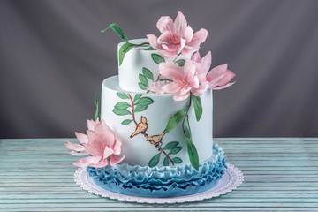 A beautiful home wedding three-tiered cake decorated with pink flowers and branches with green leaves in a rustic style.