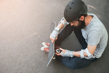 Professional skater checks his skateboard after training. First step in skateboarding sport challenge, failure and frustration, bad day for win. Skateboarder safety equipment backdrop with free space © golubovy