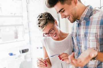 Attractive young couple in optical store buying glasses and smiling