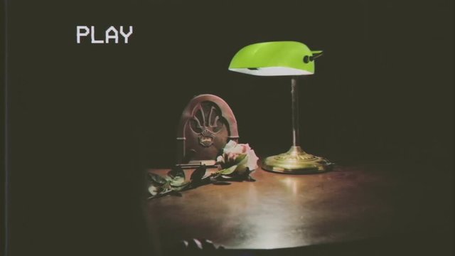 Fake VHS tape: still life with vintage objects on a table - a radio, a lamp, a yellow rose with blood stains over its petals.
