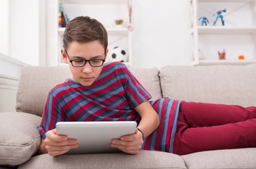 Teenage boy using digital tablet on couch at home