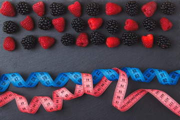 Red raspberries, blackberry and the tape measure on the black slate stone background