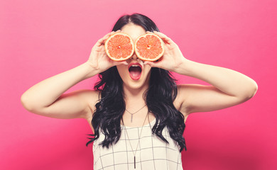 Happy young woman holding oranges on a pink background
