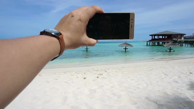 Point of View of Hand taking photo with smart phone. feet and ocean vacation background