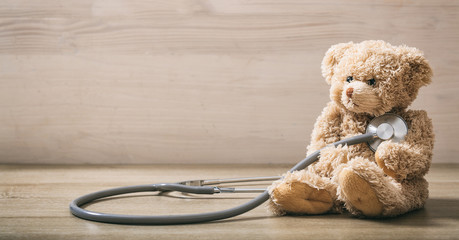 Teddy bear and a stethoscope on a wooden floor - obrazy, fototapety, plakaty