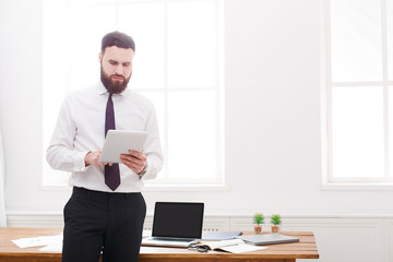 Young concentrated businessman in white shirt and tie standing and reading documents