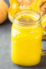 Mason glass jar with raw vegan pumpkin butternut squash smoothie with bananas, peaches, pie spices. Ingredients on dark stone background. Healthy drink. Fall.