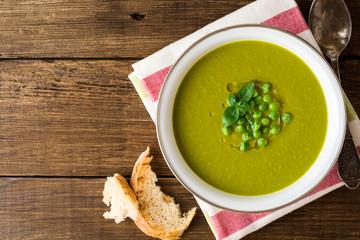 Green pea soup in bowl on wooden table