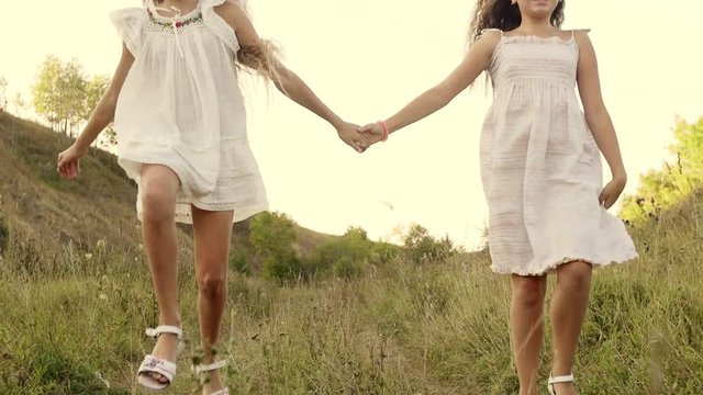 Close up view of happy children in a white dresses dancing, whirling and laughing. Close up view of two little girls whirling in a round dance in a bright sunset. Cute smiles. Childhood games.