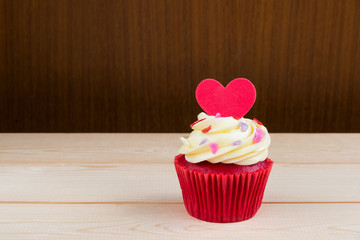Red Velvet cup cake with red heat shape sugar cube over light wood board and dark wooden background...