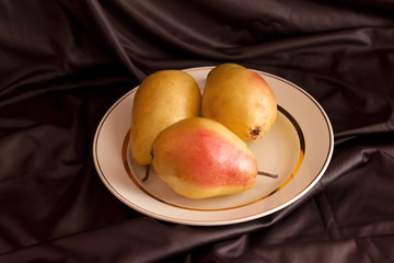 Pears on a white porcelain dish on brown satin