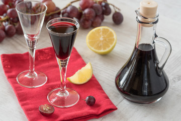 Homemade liqueur in glass and bottle with fresh grapes in background.