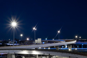 City highway in dark blue night with lamp post lighting and car park
