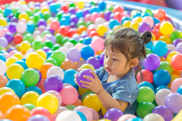 Fototapeta na wymiar Cute Asian baby girl holding purple ball in colorful plastic ball pool