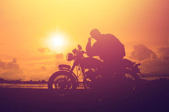Silhouette of man and a motorcycle with sunset background.