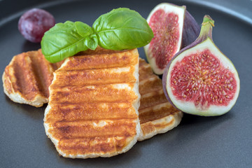 Grilled slices of halloumi cheese served on the plate with fig, grapes and basil leaf. Halloumi is popular in Cyprus, Greece, and Turkey.
