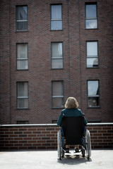 lonely woman on wheelchair surrounded by bricked buildings