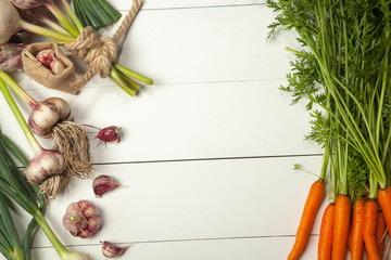 Fresh vegetables, garlic, onions and carrots on a white wooden table. View from above.