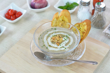 Mushroom cream soup served with garlic bread on cutting board and wood table.