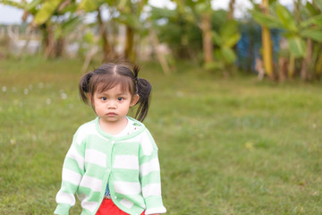 Adorable asian little girl in stripe green white color sweater looking thoughtful, distracted and unsmiling.