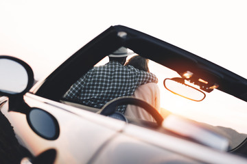 Young happy couple in love sitting on hood of cabriolet and enjoying view and sunset in mountains