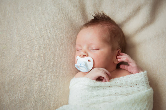 Cute newborn baby sleeping on white blanket with a pacifier