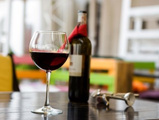 Glass of red wine with bottle and corkscrew on table in cafe