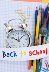 back to school concept - alarm clock and school supplies close up with back to school text on paper ribbon