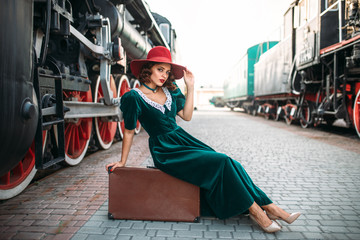 Woman sitting on suitcase against steam train