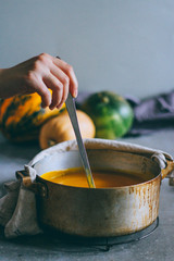 A saucepan with pumpkin soup, a poultry in his hand, stirs the soup. Autumn dish.