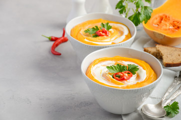 Pumpkin soup with cream and parsley on a grey concrete or stone background, selective focus, copy space