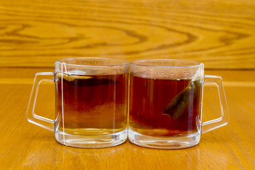 Two full glasses with rooibos tea and bag in soft focus on wooden background
