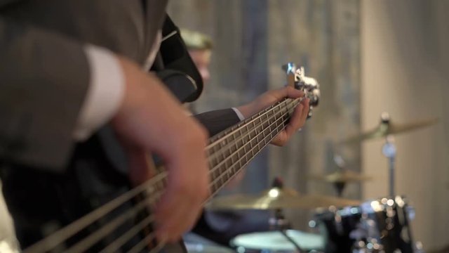 Bass guitarist in suit plays music with drummer. Black bass guitar with strings and fingers, cymbals, drums, neck, snare-drum