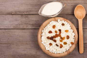 Cottage cheese in bowl with sour cream and raisins on old wooden background with copy space for your text. Top view