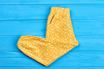 New folded trousers for baby girl. Top view of yellow infant girl trousers on blue wooden background. Kids fashion outfit.