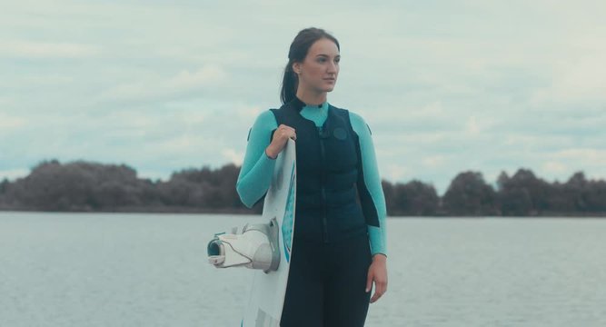 4K CINEMAGRAPH - seamless loop. Attractive female posing in a swimsuit with a wakeboard on a lake, cloudy sky