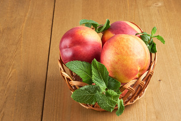 peaches in a wicker basket on wooden table with blurred background