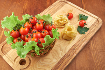 Tomatoes in a wicker basket and green leaves of salad, pasta nests on a wooden Board