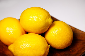 Four ripe fresh lemons on a wooden plate on a white background