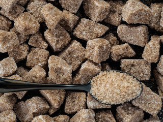 natural raw brown cane sugar cubes and granulated brown sugar in spoon close up as background. Top view of brown sugar with copy space