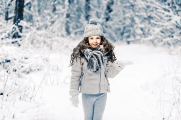 Fototapeta na wymiar Beautiful child stretches her hand to catch falling snowflakes.
