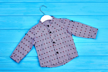 Baby boy grey dotted cotton shirt. New fashionable kids wear on blue wooden background. New cotton apparel for baby-boy.