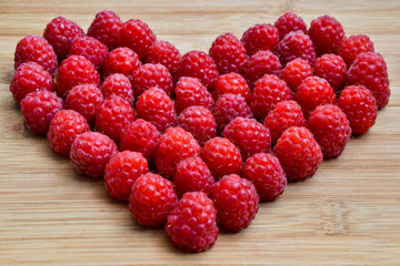 Raspberry heart. Valentines day background. Fresh raspberries from village garden. Love berries symbol for desserts, cakes, smoothie or jam on wooden texture.