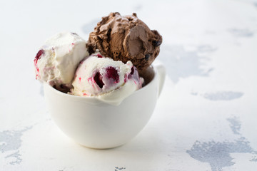 Chocolate and vanilla ice cream with berries on white table in porcelain cup. Space for text