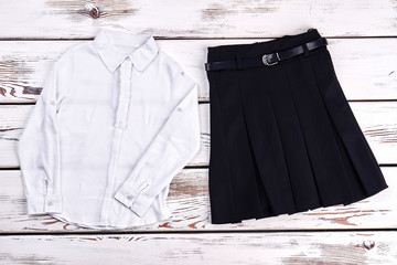 Girls school uniform, top view. White cotton shirt and black pleated skirt for school wear, old...